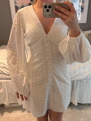 Vit broderad kortklänning Bubbleroom - Superfin vit kortklänning från Bubbleroom med broderade blommor, v-ringning och långa puffärmar. Klänningen har knappar framtill och är gjord i bomull, vilket gör den både luftig och bekväm. Perfekt för sommarens alla tillfällen! Har aldrig använts, så prislapp sitter kvar! Köpt för 699kr.