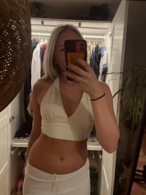 Vit halterneck linnetopp - Säljer en vit halterneck topp i linnematerial. Toppen är croppad, har v-ringning och knyt i ryggen för en öppen rygg-look. Perfekt för varma dagar och ger en fräsch och trendig stil. Passar flera storlekar då man kan knyta både i rygg och hals!