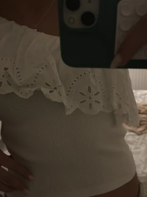 Vit offshoulder topp med volang - Hade sagt som storlek xxs eller 160 ish då de inte finns nån lapp..Supersöt vit offshoulder topp med bred volangkant och broderade blommönster. Toppen är ribbad i tyget och har en romantisk vibe, perfekt för varma dagar. Volangen ger en extra touch och toppen sitter snyggt över axlarna.