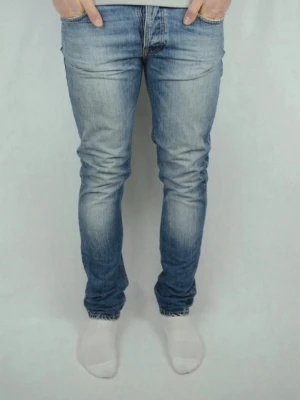 Ljusblå slim fit jeans från Nudie - Säljer ett par ljusblå slim fit jeans från Nudie med klassisk femficksmodell och snygga slitningar. Jeansen har broderade bakfickor och är tillverkade i mjuk denim med stretch för extra komfort. Perfekta för en avslappnad och trendig look.