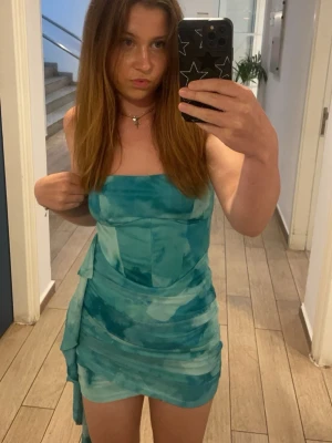 Turkos kort klänning med drapering - Säljer en snygg turkos kort klänning med draperade detaljer och raka axelband. Klänningen har en cool batikliknande effekt och sitter figurnära. Perfekt för dig som vill sticka ut med en unik look.