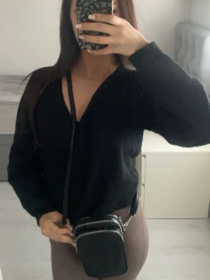 Svart axelväska med silverdetaljer - Säljer en liten svart axelväska med tre dragkedjor i silver och justerbar axelrem. Väskan har en kompakt, rektangulär form och passar perfekt för det viktigaste. Enkel och stilren design som funkar till många outfits.