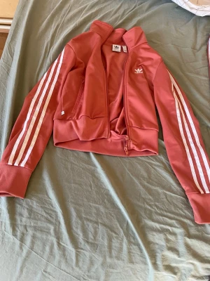 Rosa Adidas track med vita ränder - Säljer ett snyggt rosa Adidas sett använt fåtal gånger. Som ny, säljer det pga ingen användning.