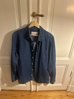 These Glory Days - Storlek: L (normal i storlek) Skick: Mycket bra skick, sparsamt använd  Beskrivning: Klassisk blå denimskjorta i tunnare material som passar till det mesta.  Hör av er vid eventuella frågor!