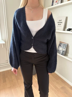 Mörkblå fluffig kofta med ballongärm - Mysig mörkblå kofta med två knappar framtill och ballongärmar. Koftan är kortare i modellen och har en mjuk, fluffig känsla. Perfekt att slänga över ett linne eller t-shirt för en avslappnad look.