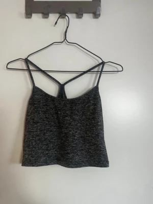 Mörkgrå croppad linnetopp - Säljer en mörkgrå croppad linnetopp med tunna axelband och snygg omlottdetalj i ryggen. Toppen har en sportig vibe och är perfekt till jeans eller kjol. Materialet känns mjukt och stretchigt, troligen polyester eller bomullsmix. Rök och djurfritt hem. Pruta gärna!🌸