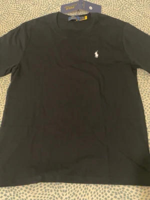 Svart t-shirt från Polo Ralph Lauren - Klassisk svart t-shirt från Polo Ralph Lauren med den ikoniska broderade loggan i vitt på bröstet. T-shirten har rund halsringning och korta ärmar. Perfekt basplagg med stilren design och skön passform.