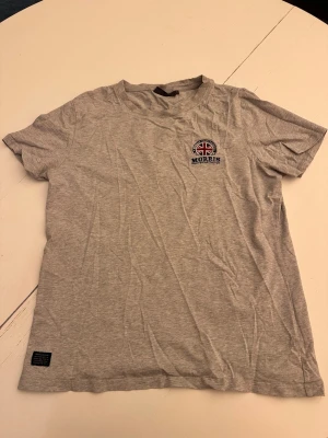 Grå t-shirt från Morris - Grå t-shirt från Morris med broderad brittisk flagga och texten 'Morris Gentlemen' på bröstet. Klassisk passform och rund halsringning, perfekt för en avslappnad stil.