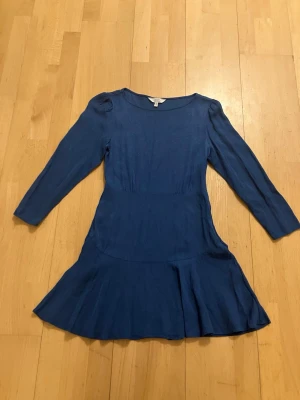 Blå klänning med volangkjol & other stories! Storlek 36 - Snygg elegant blå klänning med rund halsringning och långa ärmar. Kjolen har en volangkant som ger en feminin touch. Tillverkad i ett mjukt, lätt glansigt material som faller fint. Perfekt för dig som vill ha en enkel men stilren look. Glittriga detaljer på klänningen märke & other stories, slutsåld och finns inte inne i sortimentet just nu vad jag kan se