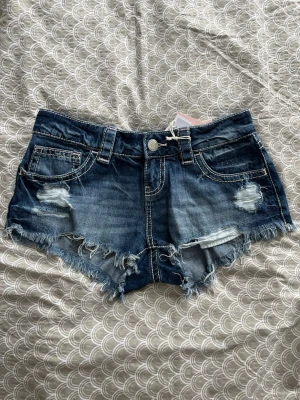 Blå jeansshorts med fransig kant - Säljer ett par blå jeansshorts från Gina Tricot i storlek XS. Shortsen har fransig kant, slitna detaljer och klassisk femficksmodell. Perfekta för sommaren och har låg midja för en avslappnad look.