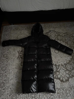 Svart lång dunjacka från Jackit - Säljer en svart lång dunjacka från Jackit med huva och dragkedja framtill.  Jag köpte jackan för 5500 nypris och säljer den för detta priset. Vid snabbköp var gärna säkra och prisförslag är alltid välkomna 