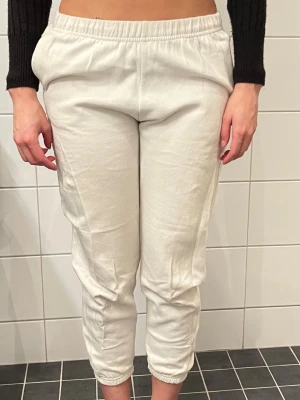 Vita mjukisbyxor med resår - Säljer ett par vita mjukisbyxor med resår i midjan och vid bensluten. Byxorna har en relaxed fit och är tillverkade i ett mjukt och bekvämt material, perfekta för chill dagar. Klassisk modell utan synligt märke och med fickor på sidorna.