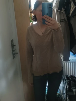 Beige stickad tröja med V-ringning - Mysig beige stickad tröja med V-ringad hals och långa ärmar. Tröjan har en avslappnad passform och är perfekt för lager på lager. Passar till både jeans och kjol för en enkel vardagslook.