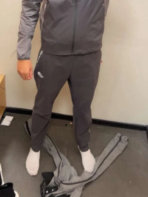 Grå mjukisbyxor från The North Face - Säljer ett par grå mjukisbyxor från The North Face med vit logga på benet. Byxorna har elastisk midja och fickor med vit och röd detalj vid dragkedjan. Perfekta för chill dagar eller när du vill ha det bekvämt.