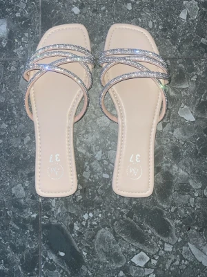 Beige sandaler med strassband - Säljer ett par snygga beige sandaler från new yorker med fyrkantig tå och flera tunna band täckta av glittrande strass. 