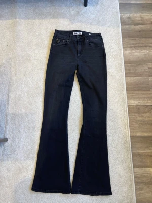Svarta bootcut jeans från Gina Tricot - Säljer ett par svarta bootcut jeans från Gina Tricot med hög midja och klassisk femficksmodell. Jeansen har utsvängda ben och är tillverkade i stretchigt denimtyg för en bekväm passform. Perfekta för en trendig och avslappnad look.