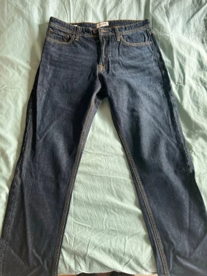Mörkblå raka jeans från Jack & Jones - Snygga mörkblå jeans från Jack & Jones med klassisk rak passform och kontrastsömmar. Jeansen har fem fickor, bälteshällor och en läderpatch med logga bak i midjan. Tillverkade i slitstark denim som passar perfekt till en avslappnad stil.