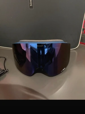 Mörk blå skidglasögon från Chimi - Säljer ett par svarta skidglasögon från Chimi med spegelblå lins och Carl Zeiss-linsteknologi. Glasögonen har magnetiskt fäste och multilager ansiktsskum för extra komfort. Perfekta för dig som vill ha stilrena och funktionella goggles i backen.