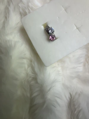 Silverringar en m rosa, en m vit sten - Snygga silverfärgade ringar med stora stenar, en rosa och en vit. Ringarna har klassiska designs med glittrande detaljer på sidorna som ger extra bling. Perfekt för dig som gillar att sticka ut med accessoarer och vill ha något unikt. Denna annons gäller 2 ringar, finns annan annons för varsin ring om man skulle vilja ha en av dem! 