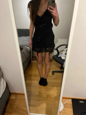 Pull&bear svart miniklänning med volang/chiffong - Säljer en svart kort klänning med tunna axelband och chiffong/volang detaljer som går diagonalt. Klänningen har ett skirt lager längst ner som ger en snygg effekt. 