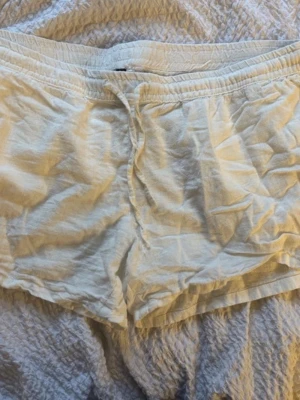 Vita linneshorts med snörning - Säljer ett par vita shorts i linne med elastisk midja och snörning framtill. De har en avslappnad passform och är perfekta för varma dagar. Klassisk och enkel design som passar till det mesta.