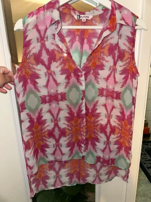Mönstrad ärmlös blus från Instinct storlek: 36 - Färgstark ärmlös blus från Instinct med ett unikt abstrakt mönster i rosa, orange, grön och vit. Blusen är tunn och luftig med krage och knappar framtill, perfekt för varma dagar och snygg till jeans eller kjol.