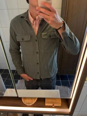 Grå overshirt från Jack & Jones - Snygg grå overshirt från Jack & Jones med två bröstfickor med lock och knappar framtill. Tillverkad i mjukt tyg som ger en avslappnad look. Perfekt att bära över en skjorta eller t-shirt för en trendig lager-på-lager stil.