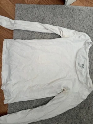 Vit långärmad topp från 157 - En enkel vit långärmad topp från 157 med rund halsringning. Tillverkad i mjuk bomull, perfekt för lager på lager eller som basplagg. Klassisk och stilren design som passar till det mesta.