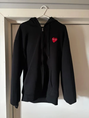 Svart hoodie Comme des Garçons Play - Svart zip hoodie från Comme des Garçons Play.Tröjan är i storlek M och är otroligt snygg och skön! Skriv vid frågor eller funderingar!