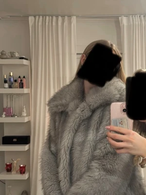 Ljusgrå fuskpäls kappa - Supermjuk och fluffig ljusgrå fuskpäls kappa med bred krage. Kappan har en klassisk rak passform och är perfekt för att hålla värmen under kyliga dagar. Snygg och trendig look som lyfter vilken outfit som helst. Använd runt 5 gånger 