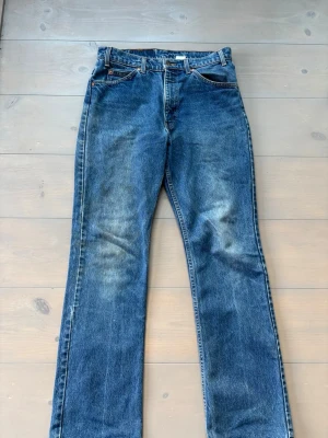 VINTAGE LEVIS 517 BOOTCUT - Klassiska blå jeans från Levi's med rak passform och fem fickor. Jeansen har en vintage tvätt med slitningar på låren och är tillverkade i kraftig denim. Perfekta för en avslappnad och tidlös stil.