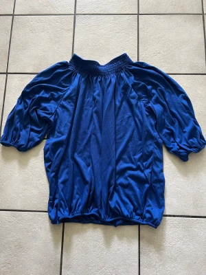 Blå blus med puffärm storlek XXL - Snygg blå blus med bred resår vid halsen och nederkanten. Blusen har puffiga trekvartsärmar och är gjord i ett mjukt, tunt tyg som känns skönt mot huden. Perfekt för dig som vill ha en trendig och bekväm look.