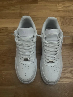 Air force 1 - Klassiska helvita Nike Air Force 1 sneakers i lågt utförande. Skorna har en stilren design med perforerad tå, vita skosnören och Nike Swoosh på sidan. Tillverkade i läder med en bekväm vadderad krage och slitstark yttersula.