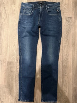 Replay Anbass Hyperflex Jeans Blå W33 - Slim Fit - Replay Anbass Hyperflex blå jeans i stretchig Hyperflex denim med slim fit passform som sitter snyggt och bekvämt och funkar till allt, storlek uppskattad W33/L okänd (innerlapp avklippt), midja 42 cm, ytterbenslängd 107,5 cm, benöppning 16 cm, modellen är 185cm & väger 65kg, i fint skick.