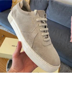 Beige mockasneakers Axel Arigato - Stilrena sneakers i beige mocka från Axel Arigato. Skorna har en klassisk låg siluett, vita snören och vit sula. Perfekta för dig som gillar minimalistisk och clean stil. Materialet är mjuk mocka som ger en exklusiv känsla.