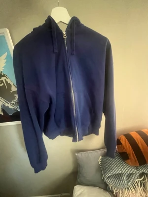 Mörkblå zip hoodie med huva - En enkel och stilren mörkblå hoodie med dragkedja framtill och stor huva. Hoodien har ribbade muddar vid ärmslut och nederkant samt två fickor framtill. Perfekt för en chill och avslappnad look. Materialet känns mjukt och bekvämt, troligen bomullsblandning.