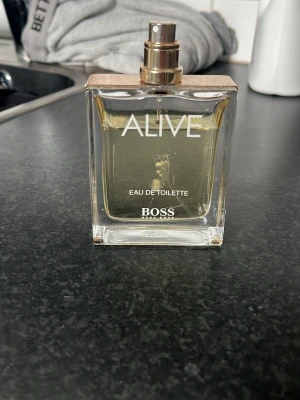 Hugo Boss Alive Eau de Toilette - Fräsch parfym från Hugo Boss, Alive Eau de Toilette. Flaskan är rektangulär i genomskinligt glas med guldig spraytopp och träfärgat lock. Doften är modern och passar dig som gillar eleganta och fräscha toner.