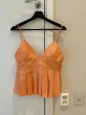 Ny trendig Randig orange linnetopp med smala axelband - Säljer en söt orange linnetopp med vita smala ränder och tunna axelband. Toppen har v-ringad hals och lätt utsvängd passform nedtill. Perfekt för varma dagar och enkel att styla med jeans eller kjol.
