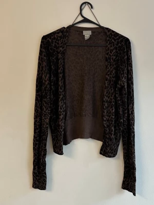 Leopardmönstrad brun kofta Gina Tricot - Snygg brun kofta från Gina Tricot med leopardmönster. Koftan har långa ärmar och dekorativa knappar vid ärmsluten. Tunn och mjuk kvalitet, perfekt för lager på lager. Öppen framtill utan knäppning.