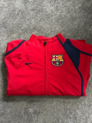 FC Barcelona Nike träningsjacka retro - Säljer en röd träningsjacka från Nike med FC Barcelona-emblem på bröstet från 2006-2007 säsongen. Jackan är köpt från Camp Nou Arena. Perfekt för dig som vill representera världens bästa fotbollslag! NYPRIS: 1000kr.