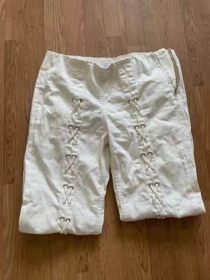 Vita leggings med snörningsdetaljer - Unika vita leggings med dekorativa snörningsdetaljer längs hela benen. Modellen har hög midja och dragkedja i sidan. Tillverkade i ett stretchigt material som ger en skön passform och trendig look.❤️