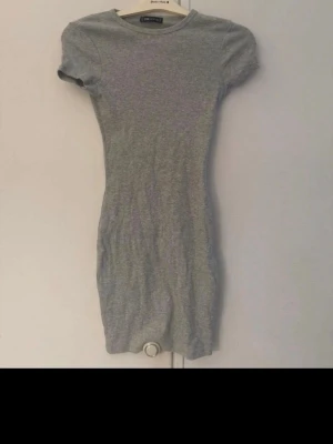 Grå ribbad kortklänning FB Sister - Säljer en enkel och stilren grå ribbad kortklänning från FB Sister i storlek XS. Klänningen har korta ärmar, rund halsringning och en tight passform som framhäver figuren. Perfekt att matcha med sneakers eller boots.