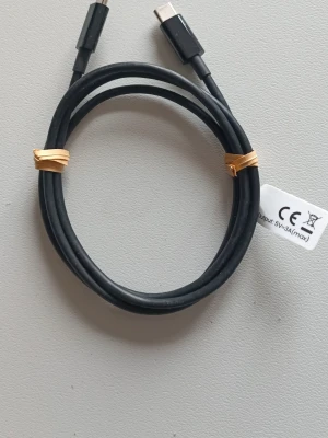 USB-C till USB-C kabel 1m - En svart USB-C till USB-C kabel, perfekt för laddning och dataöverföring mellan kompatibla enheter. Kabeln är tillverkad i slitstark plast och har en enkel, stilren design. Märkt med CE-symbol och klarar upp till 5V 3A.