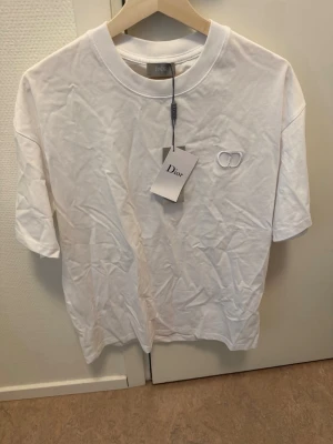 DIOR t-shirt oversize XS (fits S/M)  - Snygg vit T-shirt från Dior i bomull med broderad CD-logga på bröstet. Klassisk rund halsringning och korta ärmar. Perfekt för dig som gillar stilrena och exklusiva plagg med en lyxig touch.