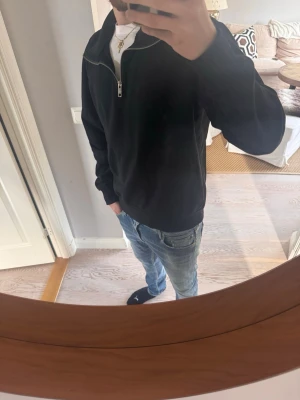 Svart halfzip sweatshirt - Svart sweatshirt med halfzip och hög krage. Tröjan har en avslappnad passform och är tillverkad i mjukt material, perfekt för en casual look. Passar bra över en t-shirt och funkar året runt.