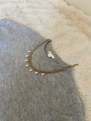 Guldhalsband med droppformade pärlor - Snyggt halsband i guldfärgad rostfritt med droppformade vita pärlor som hänger längs kedjan. Kedjan har en klassisk, lite chunky design och pärlorna ger en elegant touch. Perfekt för att lyfta vilken outfit som helst med en trendig och stilren vibe.
