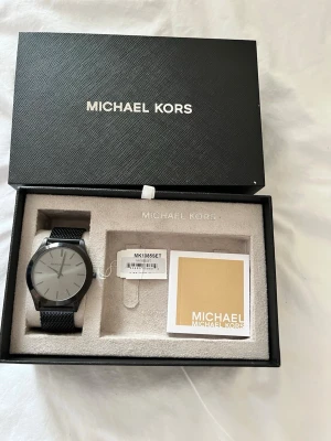 Svart mesh-klocka från Michael Kors - Stilren klocka från Michael Kors med svart mesh-armband och minimalistisk urtavla i silver. Klockan levereras i originalbox med tillhörande booklet. Perfekt accessoar för dig som gillar en clean och modern look.