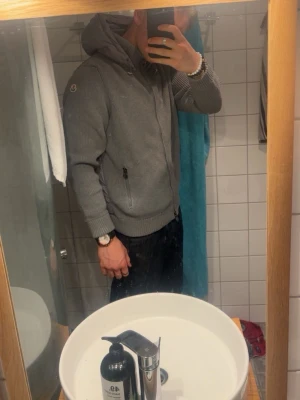 Grå hoodie från Moncler med dragkedja L - Säljer en grå hoodie från Moncler med dragkedja framtill och två fickor med dragkedja. Hoodien har ribbade muddar och en klassisk Moncler-logga på ärmen. Nyskick Storlek Large