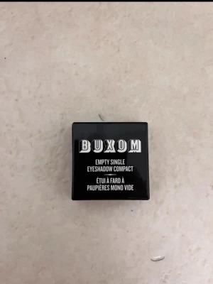 Buxom tom ögonskuggsbox - Snygg svart fyrkantig tom ögonskuggsbehållare från Buxom. Perfekt för att förvara en singelögonskugga. Kompakt design i plast med tydlig logga på locket. Smidig att ta med i väskan och enkel att fylla på med din favoritnyans. Köpte från cocopanda för 39kr. 