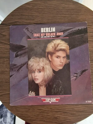 Berlin Take My Breath Away vinyl - Vinylsingel med Berlin - Take My Breath Away från filmen Top Gun. Omslaget har motiv från filmen med stridsflygplan och filmens logga. Text i vitt och rött på lila bakgrund. Producerad av Giorgio Moroder. Perfekt för dig som gillar 80-talsmusik och filmnostalgi.
